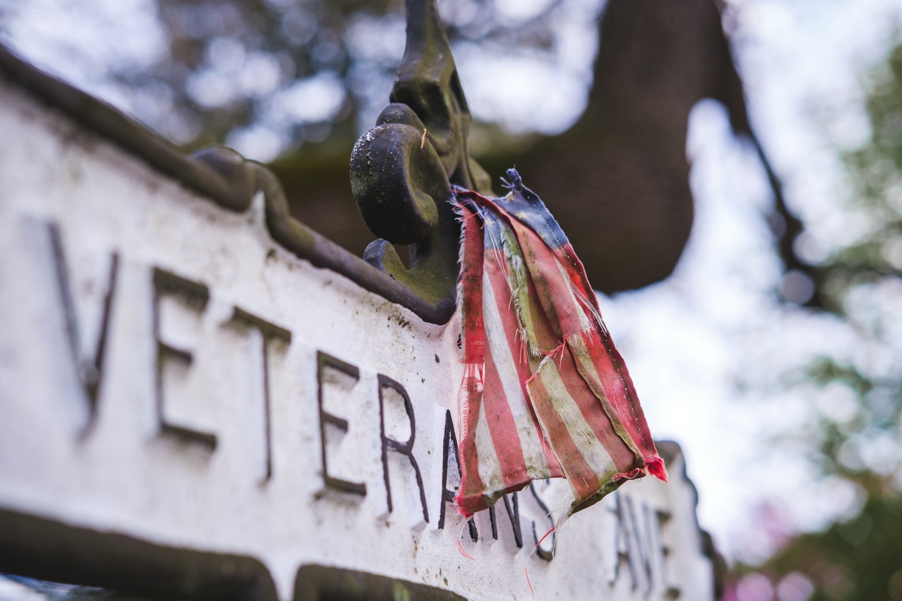 A small, worn, tattered American flag hanging on a street sign that reads 'VETERANS'.