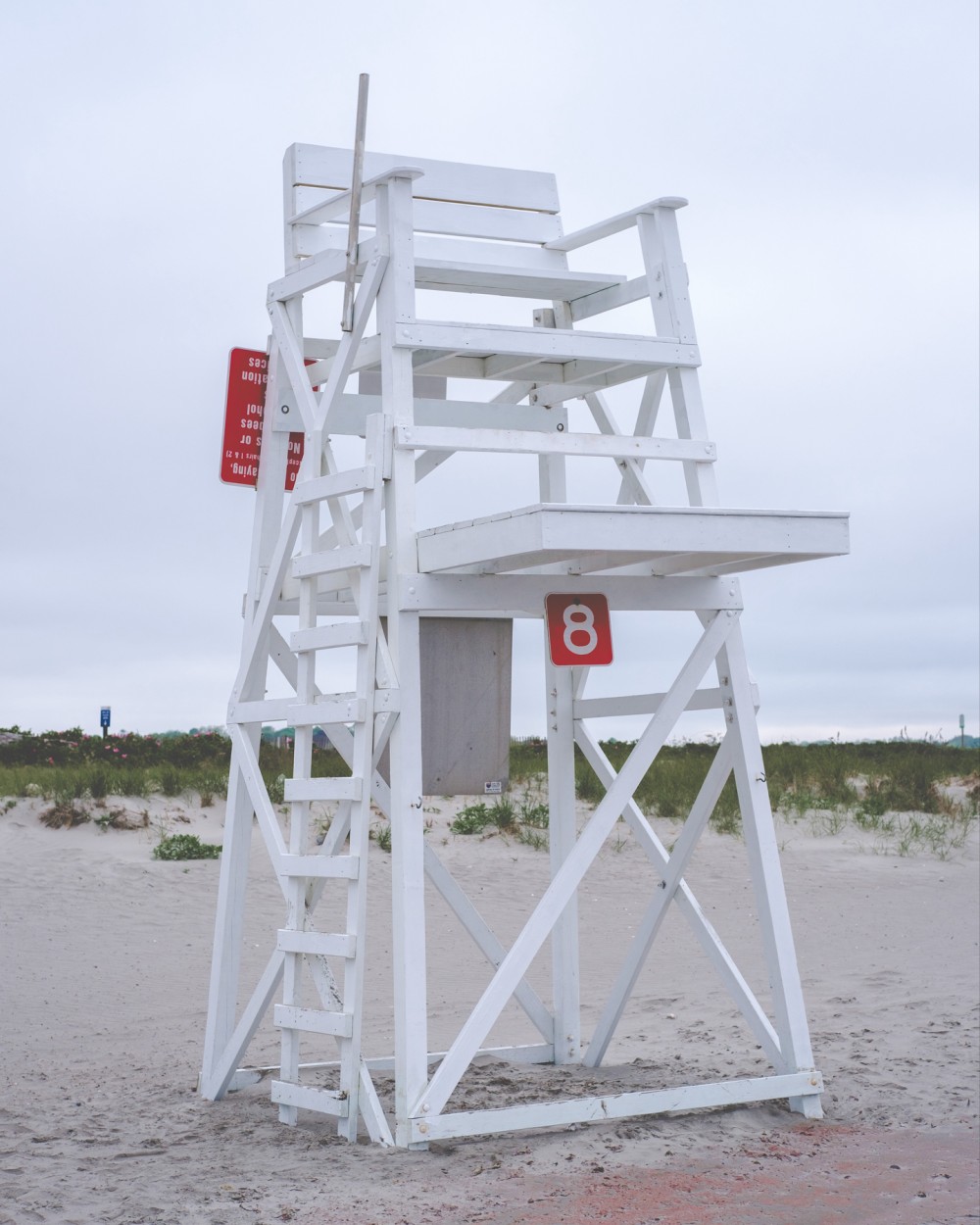 A white lifeguard tower, numbered 8, stands on a sandy beach under an overcast sky.