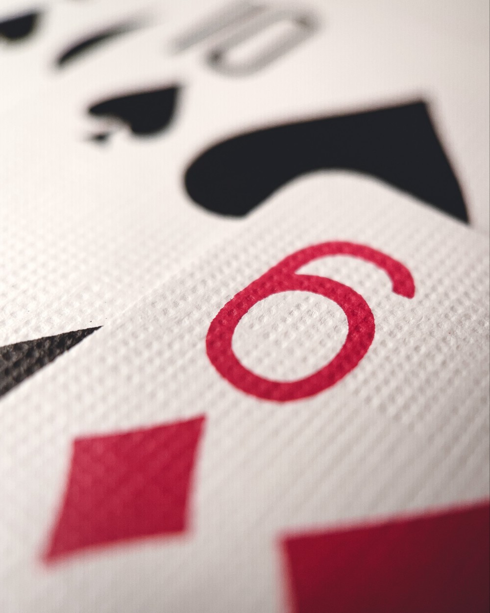 Macro photo of playing cards stacked on top of each other. 6 of diamonds is in the foreground with 10 of spades and another unidentified spades card behind it.
