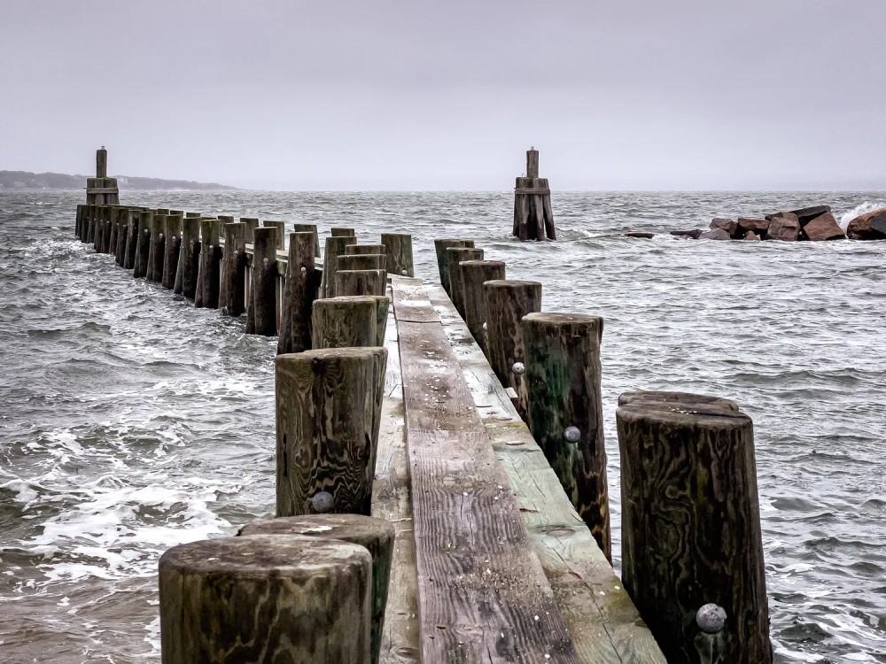 Photo of a wooden barrier with posts and planks stretching out into a stormy ocean