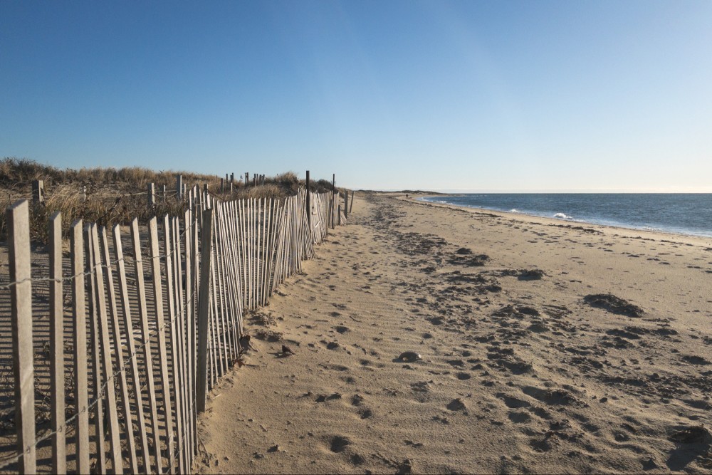 A wooden slat fence along a sandy beach and clear blue sky