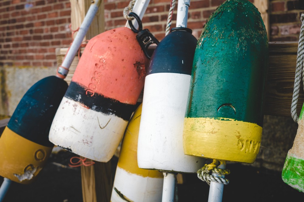 A collection of colorful, weathered buoys hanging on a wooden rack against a brick wall background.
