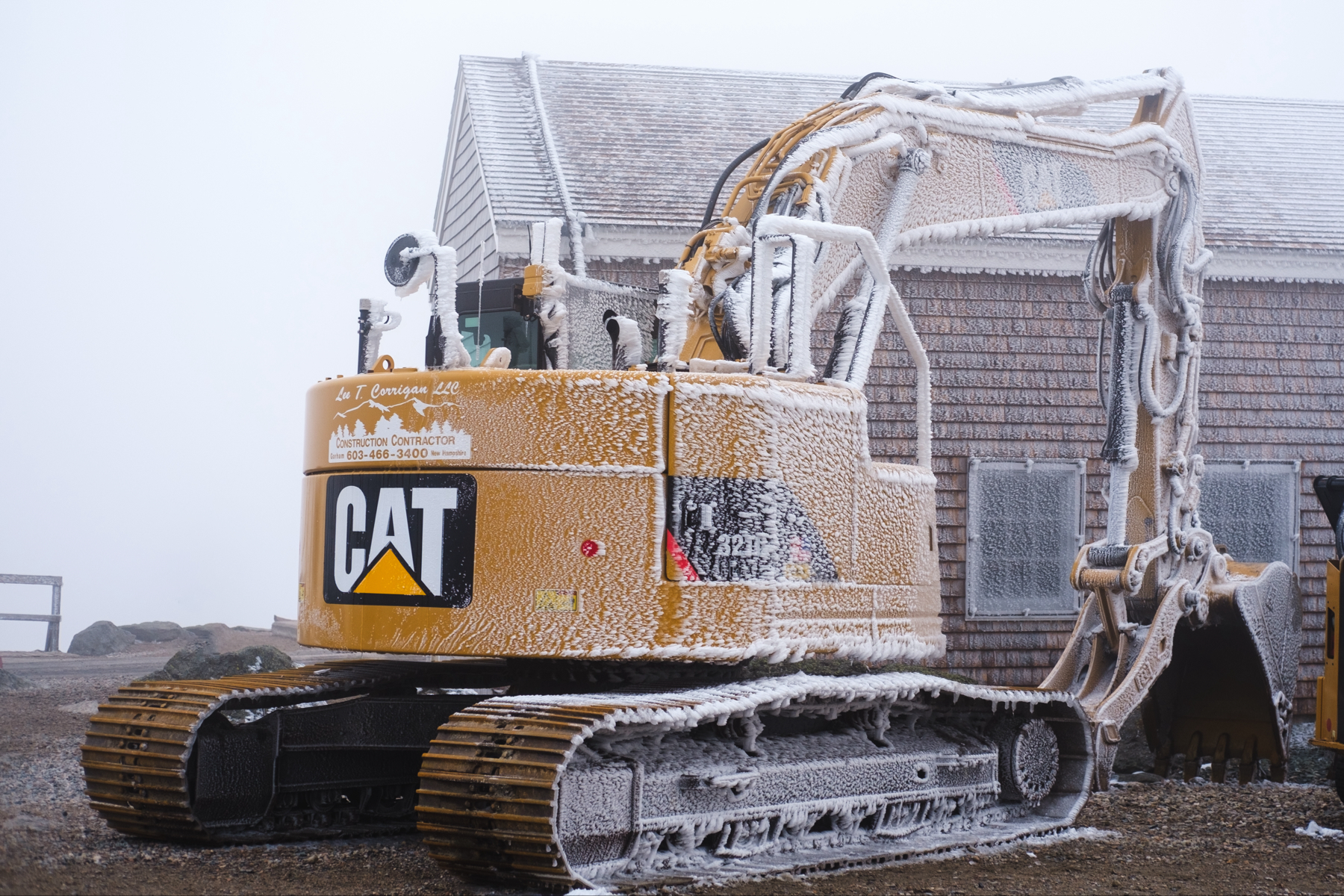 A frost-covered yellow Caterpillar (CAT) excavator next to an ice-encrusted building.