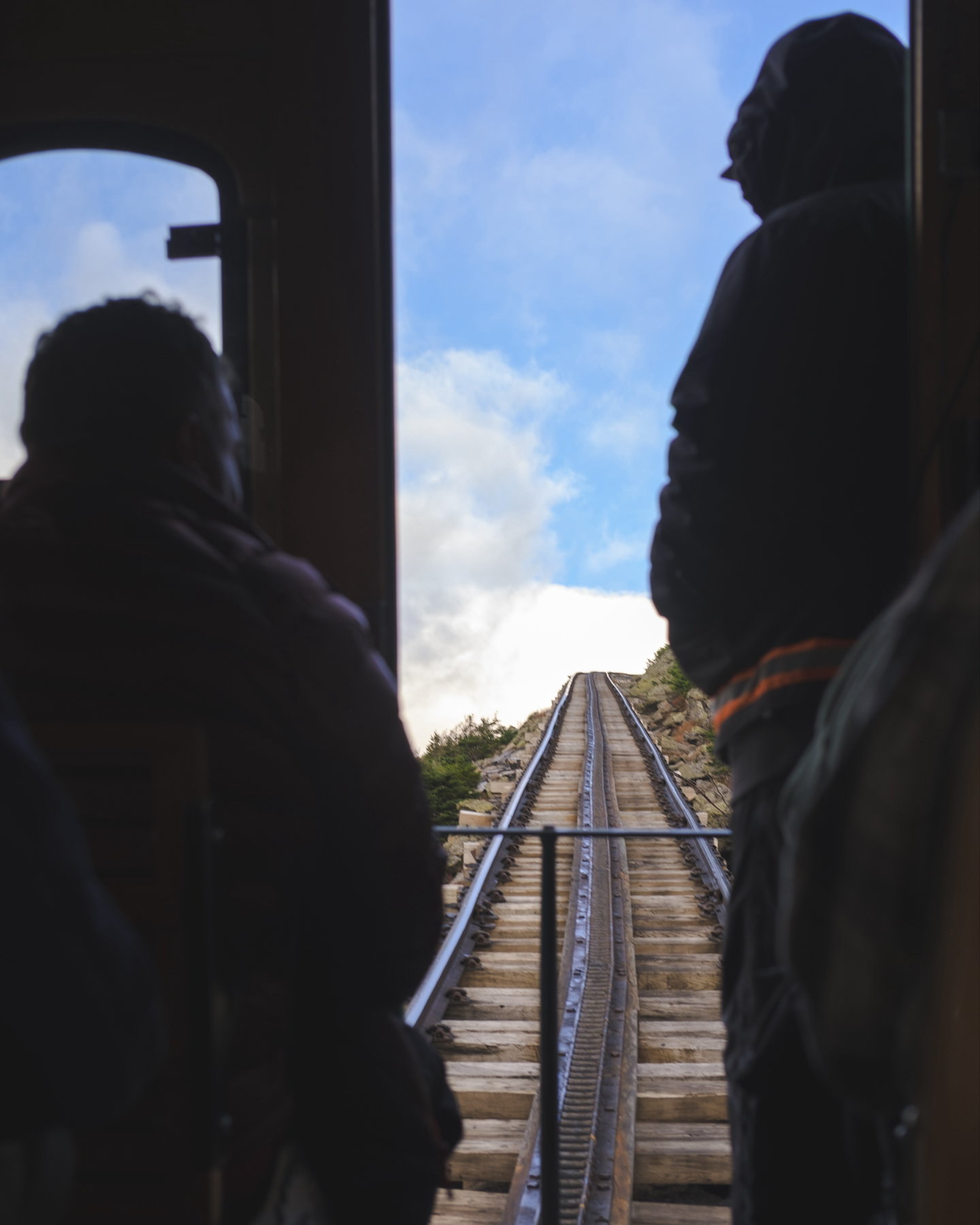 A view from inside a train looking up a steep railway track with passengers and the brakeman silhouetted against the sky.
