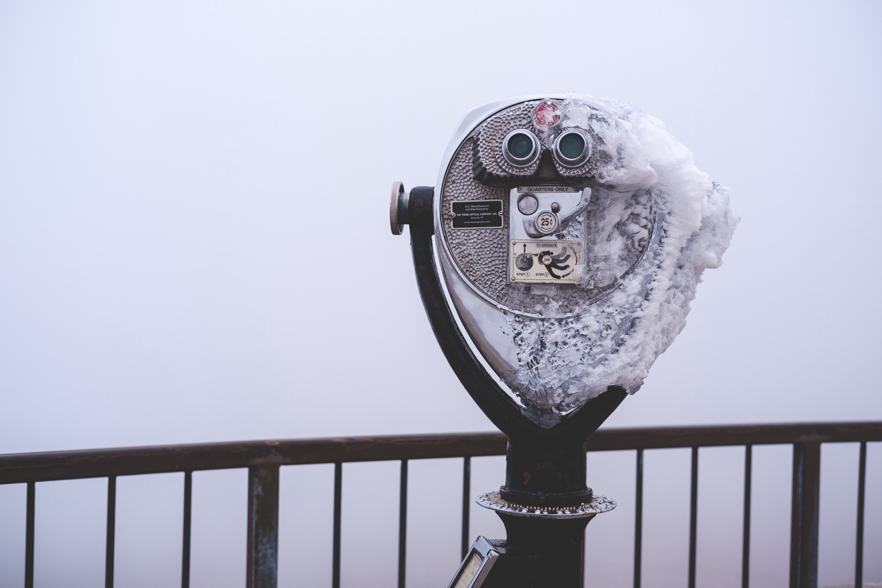 A coin-operated binocular viewer covered with ice, with a backdrop of dense fog.