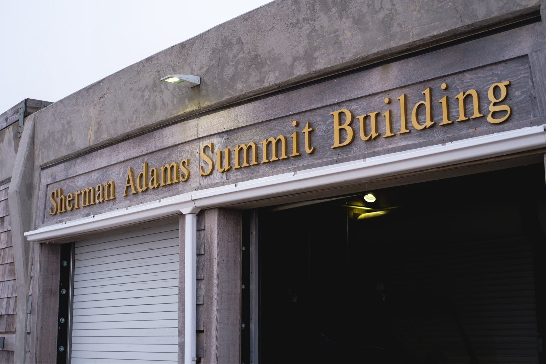 The image shows the exterior of the Sherman Adams Summit Building with its name sign displayed above a closed garage door.