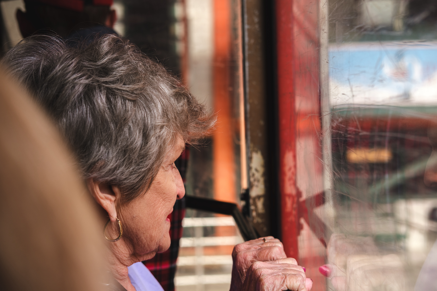 Woman with gray hair looking out of the window of a red cable car, with reflection visible on the glass.
