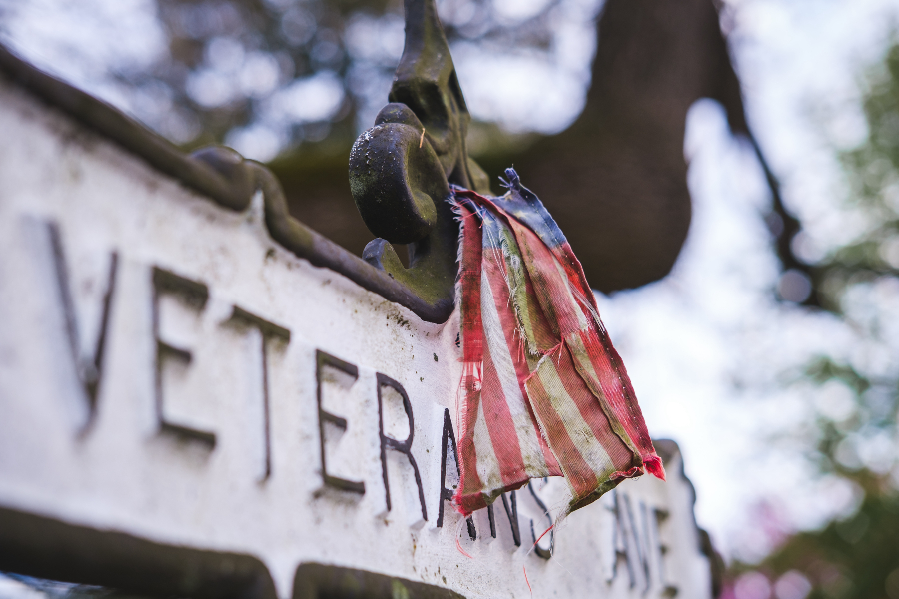 A small, worn, tattered American flag hanging on a street sign that reads ‘VETERANS’.